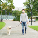 man in mask with labrador dog walking in city