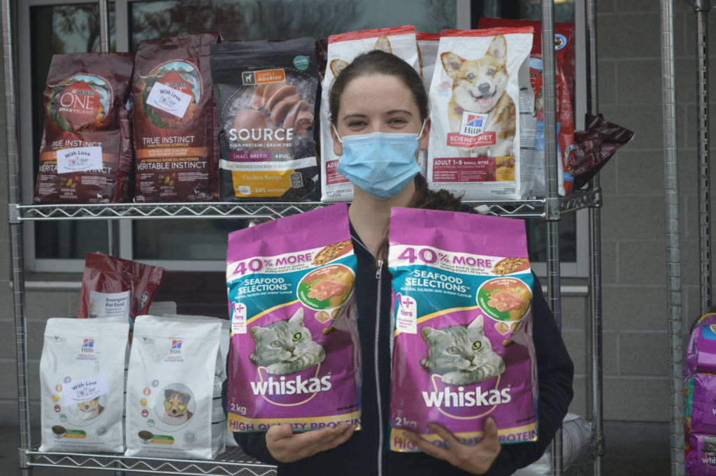 Person holding two bags of Whiskas cat food with a rack of food in the background.