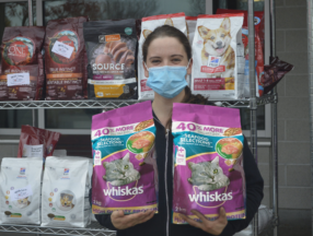 Person holding two bags of Whiskas cat food with a rack of food in the background.