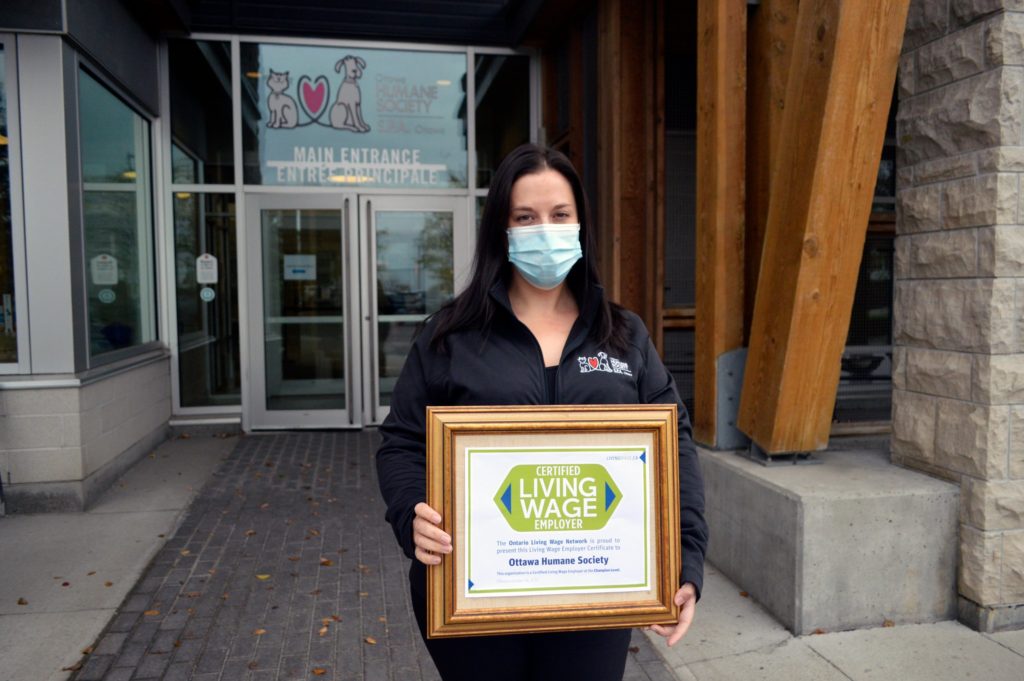 OHS employee in front of the OHS holding Living Wage plaque 